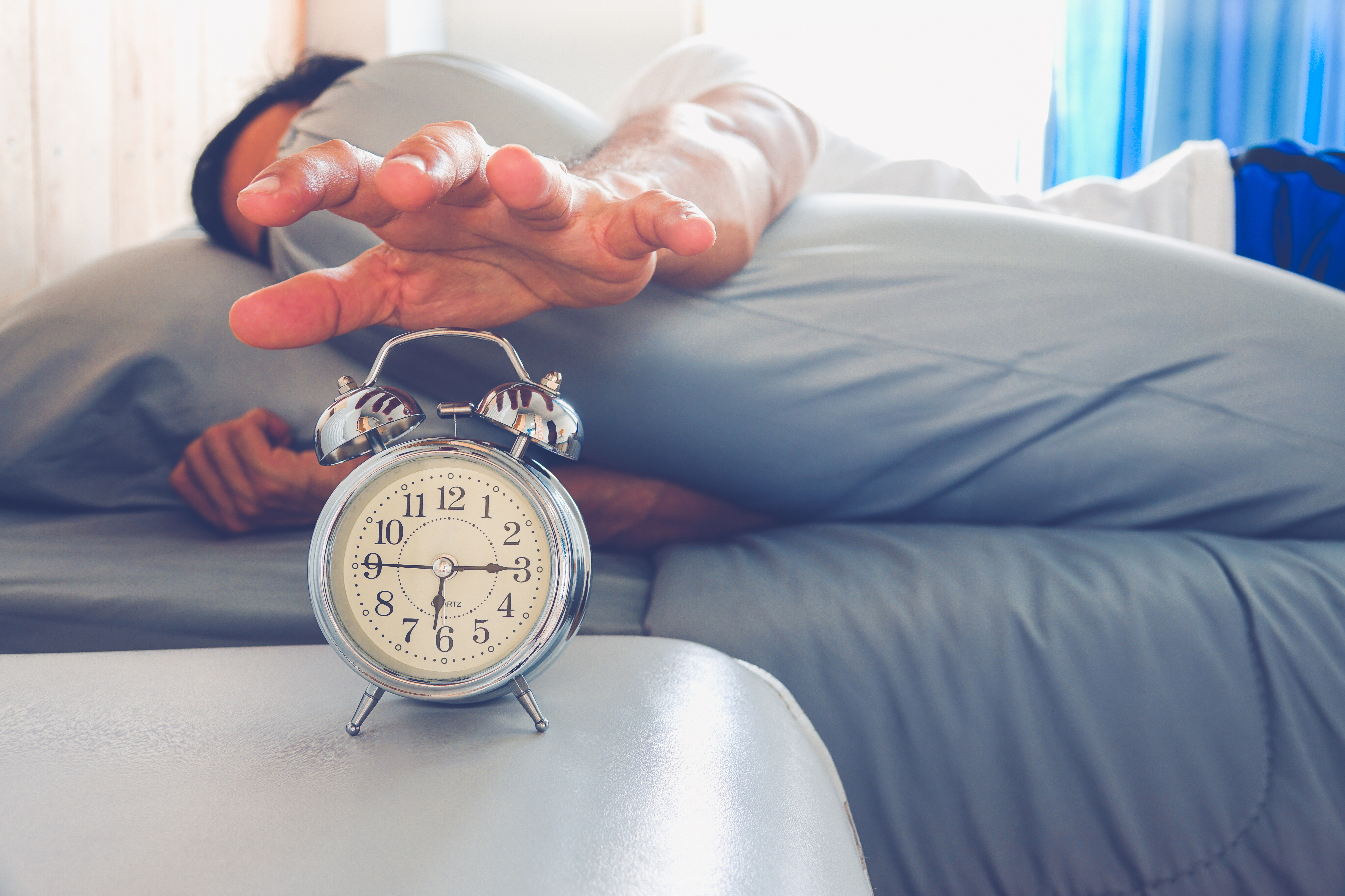 Person in bed reaching for alarm clock
