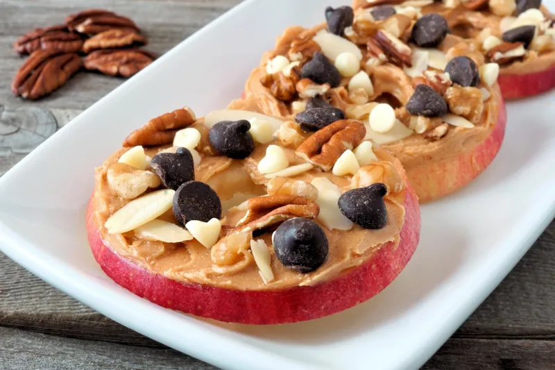 Apple slices topped with peanut butter, nuts and chocolate chips