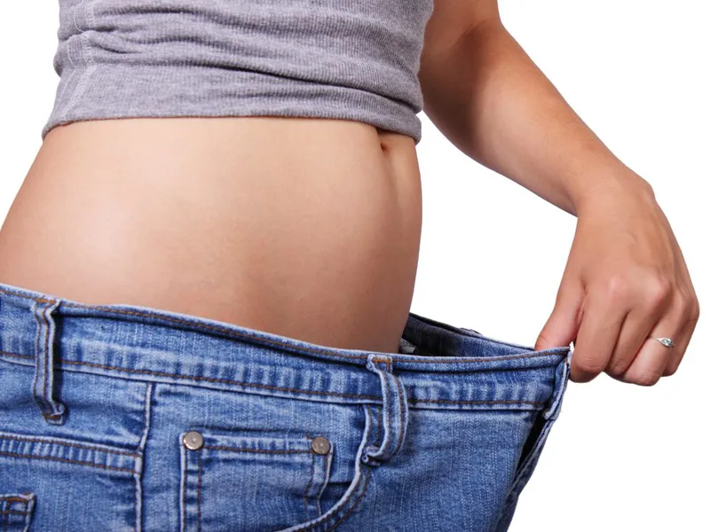 Person holding out the waistband of oversized jeans after losing weight
