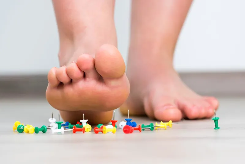 Bare foot stepping beside scattered drawing pins