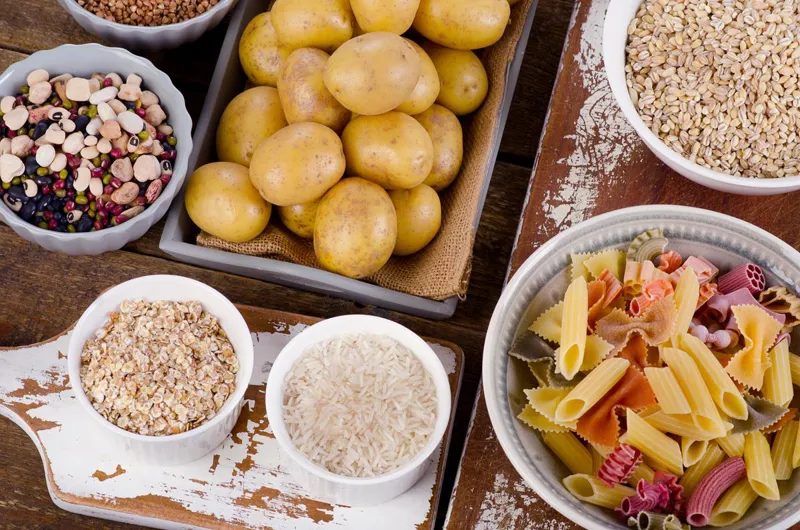 Bowls of pulses, potatoes, oats, rice, pasta and barley on a wooden table