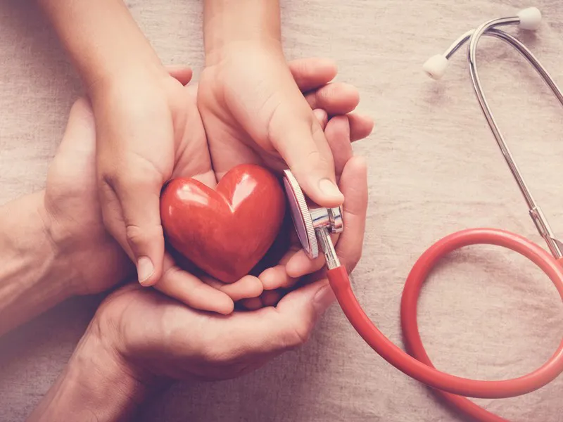 Adult and child hands holding a red heart beside a stethoscope