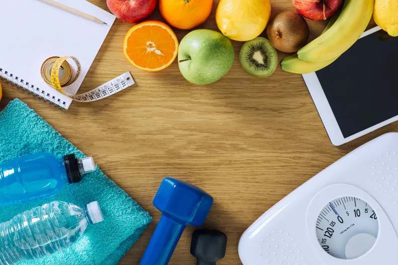 Fruit, dumbbells, water bottles and bathroom scales on a table